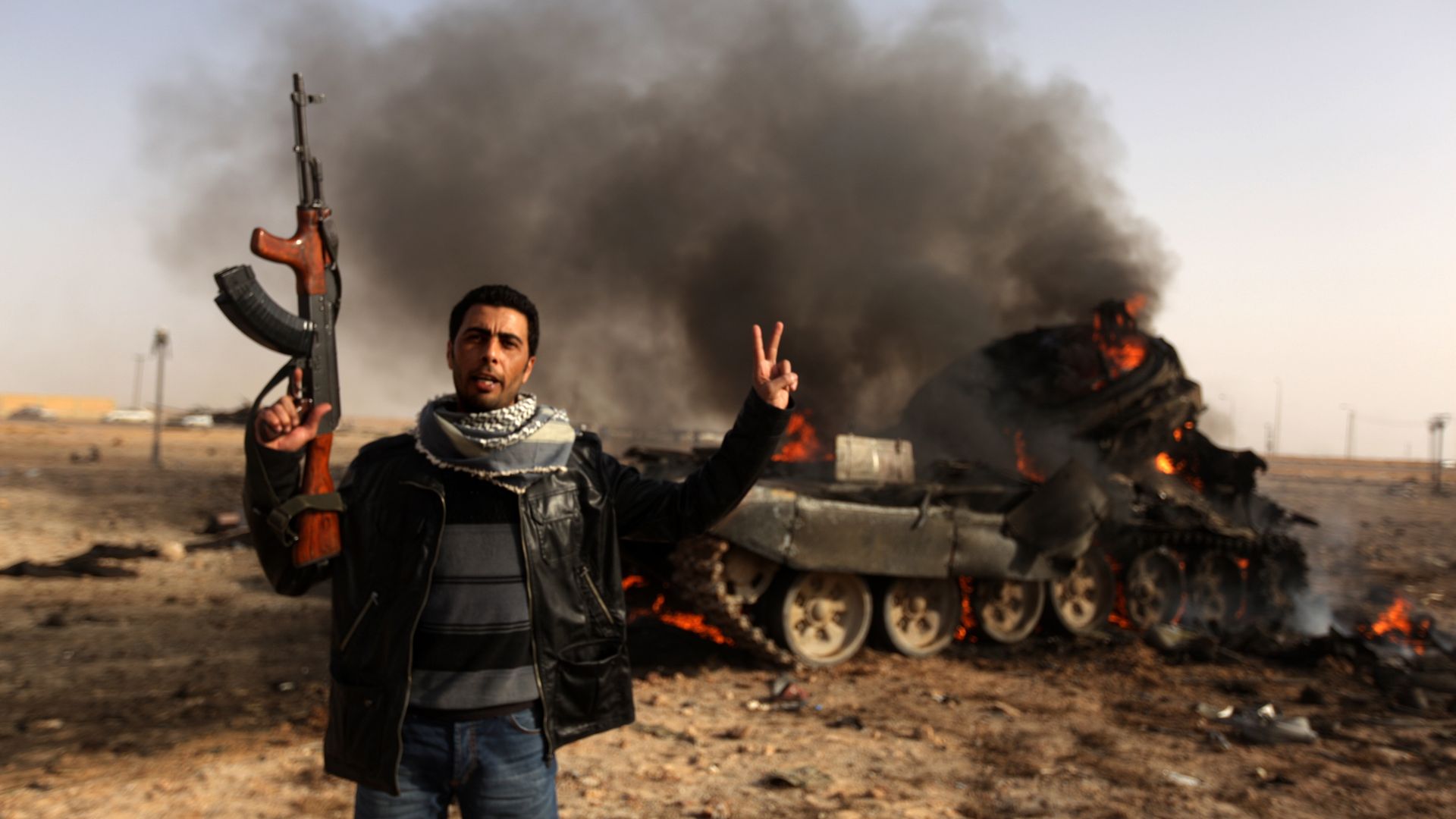 A Libyan rebel flashes a V-sign in front of burning tank belonging to loyalist forces bombed by coalition air force in the town of Ajdabiya on March 26, 2011 A Libyan rebel flashes a V-sign in front of burning tank belonging to loyalist forces bombed by coalition air force in the town of Ajdabiya on March 26, 2011 - Sputnik International, 1920, 15.02.2021