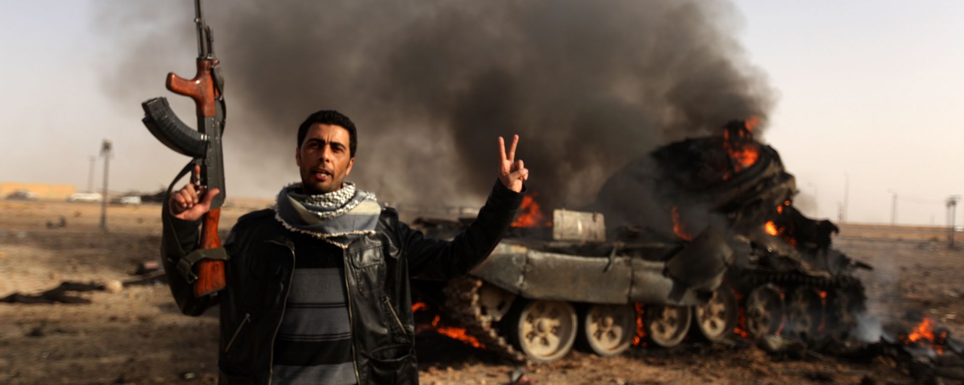 A Libyan rebel flashes a V-sign in front of burning tank belonging to loyalist forces bombed by coalition air force in the town of Ajdabiya on March 26, 2011 A Libyan rebel flashes a V-sign in front of burning tank belonging to loyalist forces bombed by coalition air force in the town of Ajdabiya on March 26, 2011 - Sputnik International, 1920, 15.02.2021