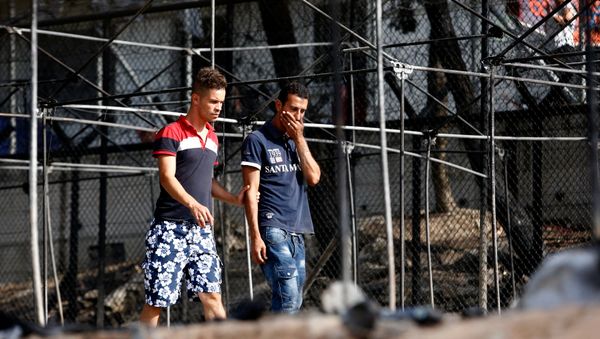 A migrant (R) reacts as he walks next to the remains of burned tents at the Moria migrant camp, after a fire that ripped through tents and destroyed containers during violence among residents, on the island of Lesbos, Greece, September 20, 2016. A migrant (R) reacts as he walks next to the remains of burned tents at the Moria migrant camp, after a fire that ripped through tents and destroyed containers during violence among residents, on the island of Lesbos, Greece, September 20, 2016. - Sputnik International