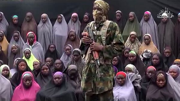 This file photo taken on August 14, 2016 shows a video grab image created on August 14, 2016 and taken from a video released on youtube purportedly by Islamist group Boko Haram showing what is claimed to be one of the groups fighters at an undisclosed location standing in front of girls allegedly kidnapped from Chibok in April 2014. This file photo taken on August 14, 2016 shows a video grab image created on August 14, 2016 and taken from a video released on youtube purportedly by Islamist group Boko Haram showing what is claimed to be one of the groups fighters at an undisclosed location standing in front of girls allegedly kidnapped from Chibok in April 2014. - Sputnik International