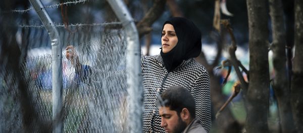 A couple stands behind a fence as refugees and migrants wait to cross the Greek-Macedonian border near the town of Gevgelija on March 3, 2016. A couple stands behind a fence as refugees and migrants wait to cross the Greek-Macedonian border near the town of Gevgelija on March 3, 2016. - Sputnik International