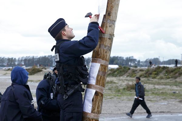 A French policeman posts the official document that announces the dismantling of the makeshift camp called the Jungle, as a migrant walks past in Calais, France, October 21, 2016 A French policeman posts the official document that announces the dismantling of the makeshift camp called the Jungle, as a migrant walks past in Calais, France, October 21, 2016 - Sputnik International