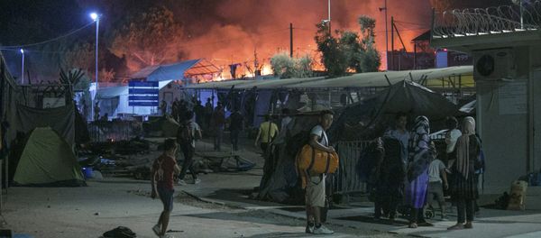 Migrants hold their belonging as a large fire burns inside the Moria refugee camp on the northeastern Greek island of Lesbos, late Monday, Sept. 19. 2016 Migrants hold their belonging as a large fire burns inside the Moria refugee camp on the northeastern Greek island of Lesbos, late Monday, Sept. 19. 2016 - Sputnik International