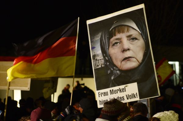 A protestor holds a poster with an image of German Chancellor Angela Merkel wearing a headscarf in front of the Reichstag building with a crescent on top during a rally of the group Patriotic Europeans against the Islamization of the West, or PEGIDA, in Dresden, Germany, Monday, Jan. 12, 2015 - Sputnik International