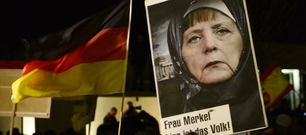 A protestor holds a poster with an image of German Chancellor Angela Merkel wearing a headscarf in front of the Reichstag building with a crescent on top during a rally of the group Patriotic Europeans against the Islamization of the West, or PEGIDA, in Dresden, Germany, Monday, Jan. 12, 2015 A protestor holds a poster with an image of German Chancellor Angela Merkel wearing a headscarf in front of the Reichstag building with a crescent on top during a rally of the group Patriotic Europeans against the Islamization of the West, or PEGIDA, in Dresden, Germany, Monday, Jan. 12, 2015 - Sputnik International