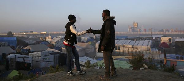 Migrants shake hands as they stand on a high point near tents and makeshift shelters on the second day of their evacuation and transfer to reception centers in France, during the dismantlement of the camp called the Jungle in Calais, France, October 25, 2016 - Sputnik International