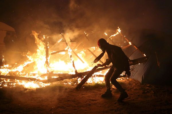 A migrant is seen in silhouette near flames from a burning makeshift shelter on the second day of the evacuation of migrants and their transfer to reception centers in France, as part of the dismantlement of the camp called the Jungle in Calais, France, October 25, 2016 - Sputnik International