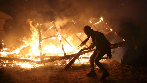 A migrant is seen in silhouette near flames from a burning makeshift shelter on the second day of the evacuation of migrants and their transfer to reception centers in France, as part of the dismantlement of the camp called the Jungle in Calais, France, October 25, 2016 - Sputnik International