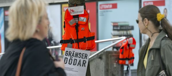 Women pass by a life vest and a placard reading Borders kill hanging on a tree in Stockholm as part of an action by Swedish branch of humanitarian NGO Doctors without borders, in solidarity with migrants seeking asylum in Europe after fleeing their home countries on September 14, 2015 - Sputnik International