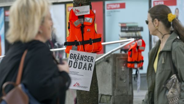 Women pass by a life vest and a placard reading Borders kill hanging on a tree in Stockholm as part of an action by Swedish branch of humanitarian NGO Doctors without borders, in solidarity with migrants seeking asylum in Europe after fleeing their home countries on September 14, 2015 Women pass by a life vest and a placard reading Borders kill hanging on a tree in Stockholm as part of an action by Swedish branch of humanitarian NGO Doctors without borders, in solidarity with migrants seeking asylum in Europe after fleeing their home countries on September 14, 2015 - Sputnik International