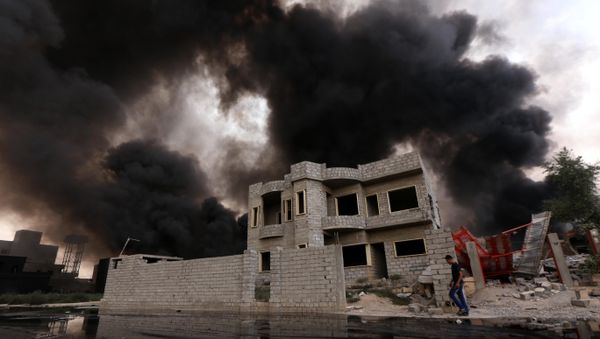 An Iraqi man walks near smoke billowing - Sputnik International