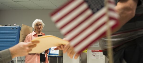 An election official watches as a man takes a ballot at an in-person absentee voting station in Fairfax, Virginia on October 12, 2016 - Sputnik International