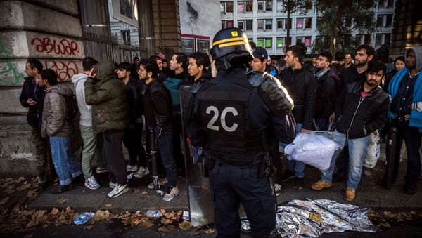 A French anti-riot policeman stands in front of migrants near the Jaures and Stalingrad metro stations, in northern Paris on October 31, 2016, during a police operation aiming at a future evacuation of a migrant camp - Sputnik International