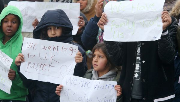 Young migrants pose with posters reading 'We want to go faster to UK' and 'We have family waiting for us' at the Jungle migrant camp in Calais, northern France, on October 26, 2016. - Sputnik International