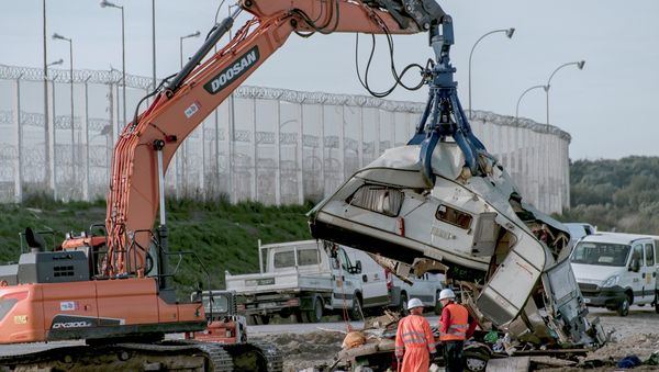 Workers watch as a crane destroys a caravan, once used as a makeshift shelter, at the site of the 'Jungle' migrant camp, on October 31, 2016 in Calais, northern France, as a massive operation to clear the settlement nears completion - Sputnik International