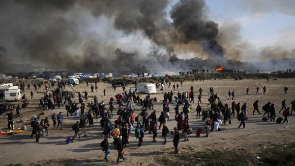 Oct. 26, 2016 file photo people walk past as thick smoke and flames rise from amidst the tents after fires were started in the makeshift migrant camp known as the jungle near Calais, northern France. Oct. 26, 2016 file photo people walk past as thick smoke and flames rise from amidst the tents after fires were started in the makeshift migrant camp known as the jungle near Calais, northern France. - Sputnik International
