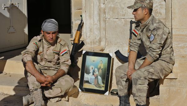Iraqi Christian soldiers from the Nineveh Plain Protection Unit, sit next to a poster showing the Virgin Mary and Jesus Christ outside St. Addai church which was damaged by Islamic State fighters during their occupation of Keramlis village, less than 18 miles, 29 kilometers, southeast of Mosul, Iraq, Sunday Nov. 13, 2016 Iraqi Christian soldiers from the Nineveh Plain Protection Unit, sit next to a poster showing the Virgin Mary and Jesus Christ outside St. Addai church which was damaged by Islamic State fighters during their occupation of Keramlis village, less than 18 miles, 29 kilometers, southeast of Mosul, Iraq, Sunday Nov. 13, 2016 - Sputnik International