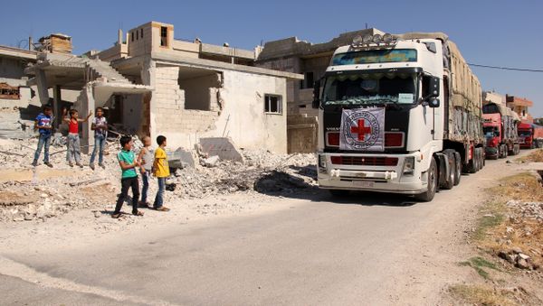 Syrian children stand on the side of a road watching a 48-truck convoy from the ICRC, SARC and UN driving through the Syrian rebel-held village of Teir Maalah, on the northern outskirts of Homs in central Syria, as it heads to the besieged town of Talbisseh on July 26, 2016 - Sputnik International