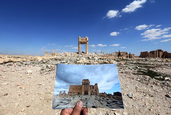 A general view taken on March 31, 2016 shows a photographer holding his picture of the Temple of Bel taken on March 14, 2014 in front of the remains of the historic temple after it was destroyed by Islamic State (IS) group jihadists in September 2015 in the ancient Syrian city of Palmyra - Sputnik International