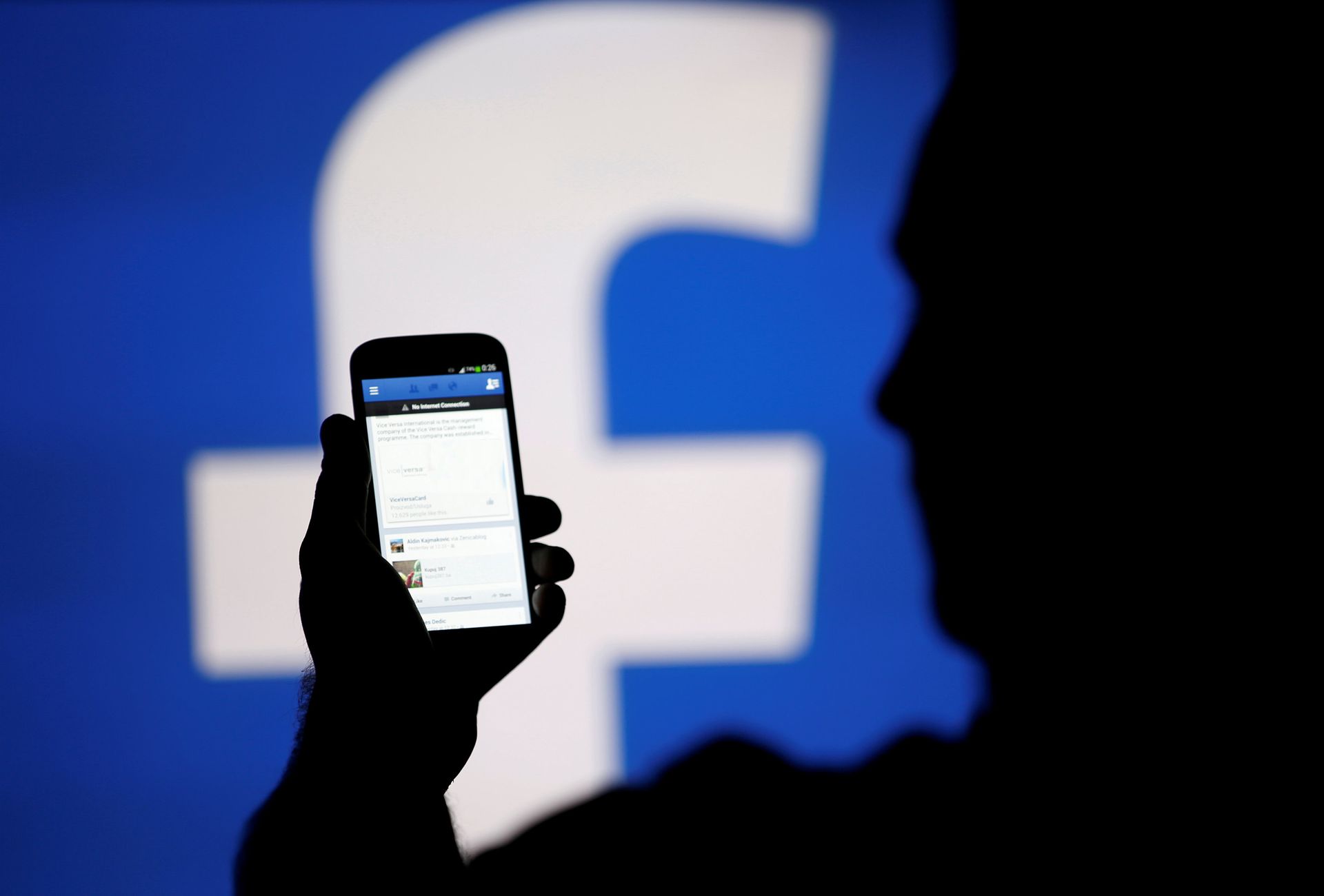 A man is silhouetted against a video screen with a Facebook logo - Sputnik International, 1920, 13.10.2021