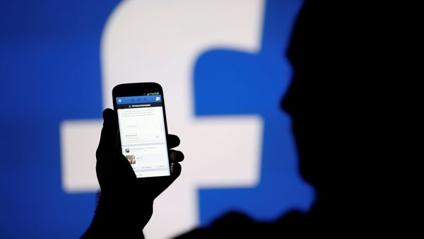 A man is silhouetted against a video screen with a Facebook logo - Sputnik International