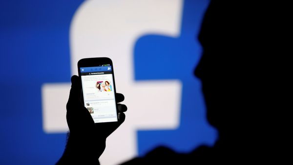 A man is silhouetted against a video screen with a Facebook logo as he poses with a smartphone in this photo illustration taken in Zenica. - Sputnik International