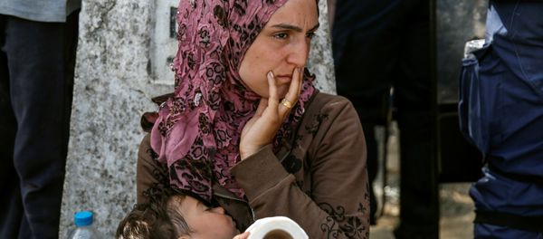 A woman sits with her child after migrants and refugees tried to open the border fence at a makeshift camp at the Greek-Macedonian border near the village of Idomeni, Greece, April 7, 2016. A woman sits with her child after migrants and refugees tried to open the border fence at a makeshift camp at the Greek-Macedonian border near the village of Idomeni, Greece, April 7, 2016. - Sputnik International