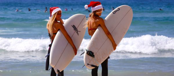 German tourists Mimi Wiebeling (L) and Pauline Lapetite carry surfboards as they walk into the surf wearing Christmas hats at Sydney's Bondi Beach on Christmas Day in Australia - Sputnik International