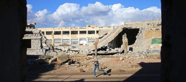 A Syrian boy runs past the rubble of destroyed buildings in the rebel-held area of Daraa, in southern Syria, on January 1, 2017 - Sputnik International