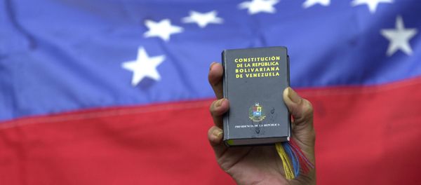 A demonstrator holds up a miniature copy of Venezuela's constitution in front of the nation's flag at a government rally in Caracas, Venezuela, Tuesday, April 13, 2004. A demonstrator holds up a miniature copy of Venezuela's constitution in front of the nation's flag at a government rally in Caracas, Venezuela, Tuesday, April 13, 2004. - Sputnik International