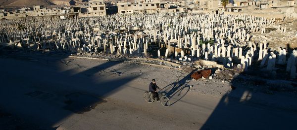 A civilian rides a bicycle past a cemetery in the rebel held besieged Douma neighbourhood of Damascus, Syria January 3, 2017 - Sputnik International