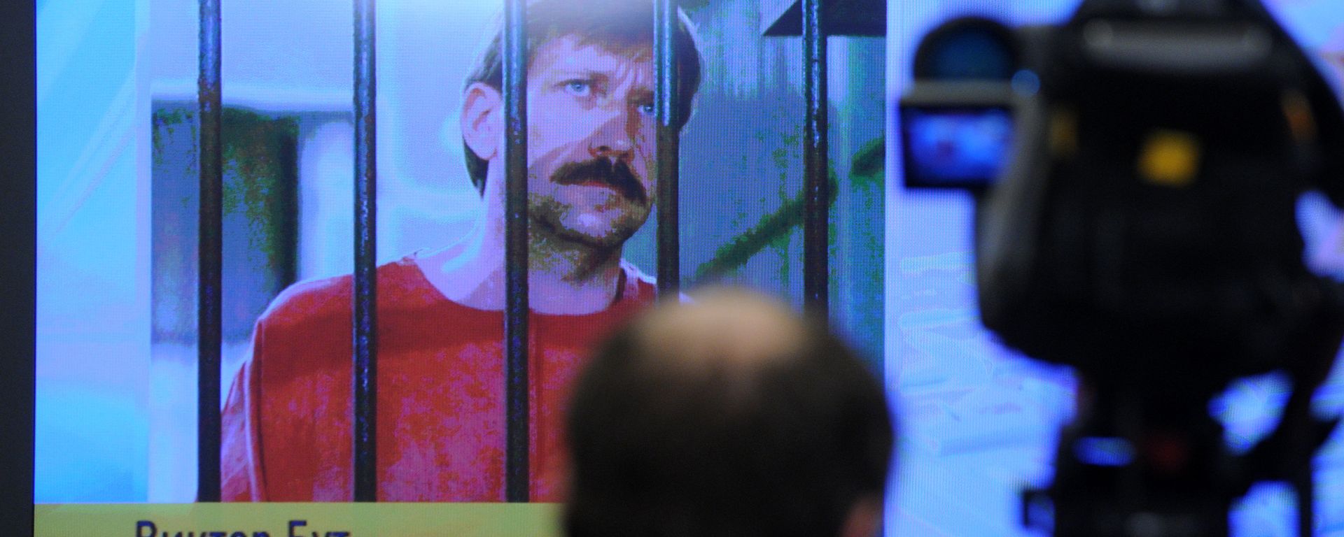 A journalist stands near a screen displaying convicted Russian arms smuggler Viktor Bout in Moscow, on 12 April 2012, during a teleconference with Bout from his US prison A journalist stands near a screen displaying convicted Russian arms smuggler Viktor Bout in Moscow, on 12 April 2012, during a teleconference with Bout from his US prison - Sputnik International, 1920, 26.10.2020