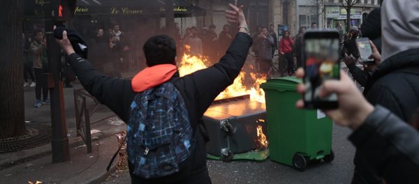A young man gestures in front of burning dustbins which obstruct the street, during a protest of students against police brutality, following the alleged rape of Theo, next to the Lycee Voltaire secondary school in Paris, on February 23, 2017 - Sputnik International