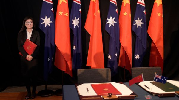 A woman holding a copy of the free trade agreement (FTA) stands next to national flags of China and Australia (File) - Sputnik International