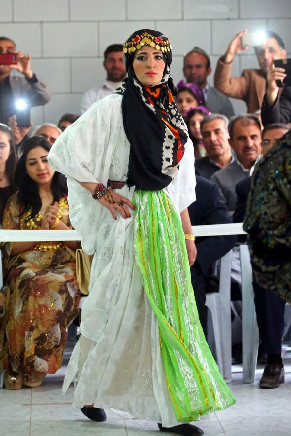 A Syrian-Kurdish model wears a full-length white gown with exaggerated sleeves and a delicate green overlay. Her head is covered in a black and gold headpiece. A Syrian-Kurdish model wears a full-length white gown with exaggerated sleeves and a delicate green overlay. Her head is covered in a black and gold headpiece. - Sputnik International