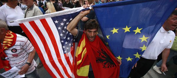 A protestor holds the flags of the United States, Macedonia, Albania and the European Union while attending a march through downtown Skopje, Macedonia, Monday, April 18, 2016 - Sputnik International