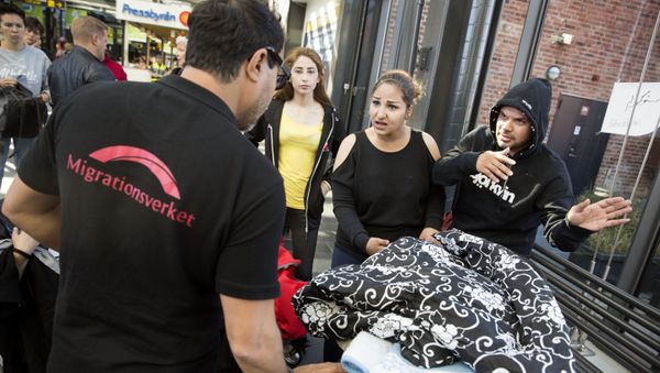 In this Sept. 8, 2015 file photo, a representative of the Swedish Migration Agency 'Migrationsverket', left, helps a migrant family from Syria as they arrive at the train station in Malmo, Sweden. - Sputnik International