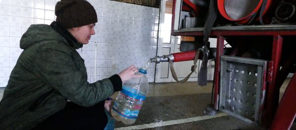 A woman in the Kievsky district of Donetsk gathers process water at the fire station after shelling - Sputnik International