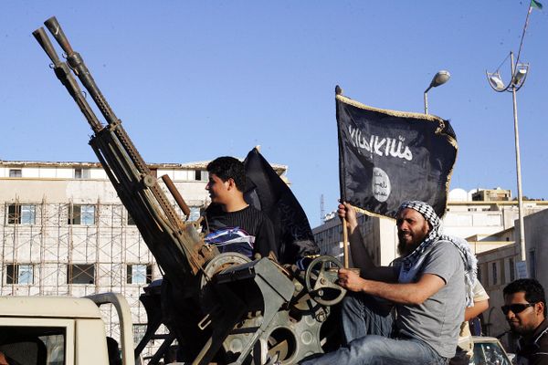 Libyan men hold Al-Qaeda flags while sitting next to an anti-aircraft artillery weapon (File) - Sputnik International