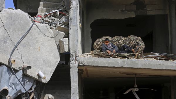 Mohammed Keferna, 14, sits on a couch in his family's building that was damaged by Israeli strikes during last summer's Israel-Hamas war, in Beit Hanoun, northern Gaza Strip, Friday, Jan. 30, 2015 - Sputnik International