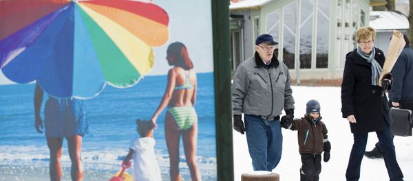 People walk along a snow covered street past an advertisement featuring a pictures of a beach scene in Mariehamn. (File) People walk along a snow covered street past an advertisement featuring a pictures of a beach scene in Mariehamn. (File) - Sputnik International