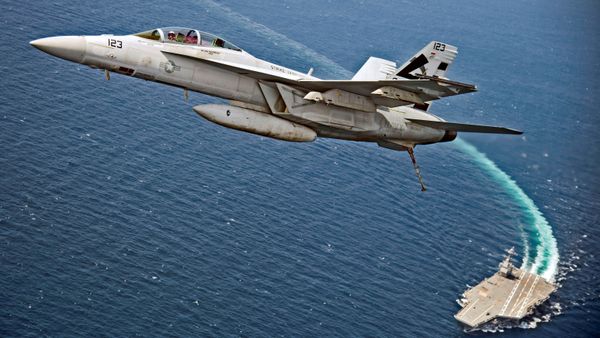 An F/A-18F Super Hornet jet flies over the USS Gerald R. Ford as the U.S. Navy aircraft carrier tests its EMALS magnetic launching system, which replaces the steam catapult, and new AAG arrested landing system in the Atlantic Ocean - Sputnik International