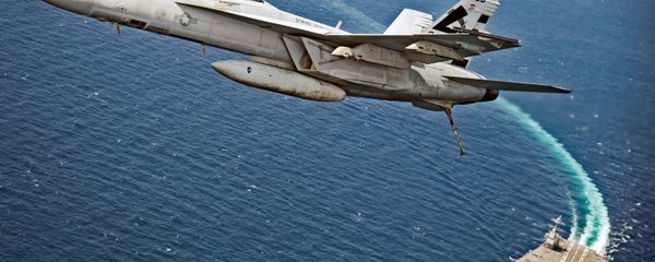 An F/A-18F Super Hornet jet flies over the USS Gerald R. Ford as the U.S. Navy aircraft carrier tests its EMALS magnetic launching system, which replaces the steam catapult, and new AAG arrested landing system in the Atlantic Ocean - Sputnik International