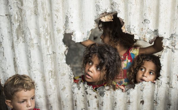 Palestinian children look through a hole in a sheet metal fence outside their home in a poor neighbourhood in Gaza City - Sputnik International