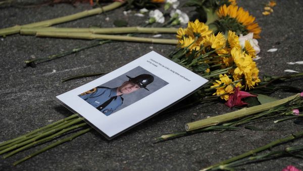 A photo of one of two Virginia state troopers killed in a helicopter crash lies among flowers at a makeshift memorial at the scene of where a car plowed into counter-protesters in Charlottesville, Virginia - Sputnik International