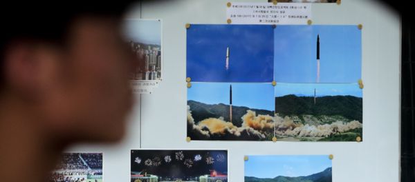 A man drives his car past a display board showing photos of ballistic missile launches in North Korea outside the North Korean Embassy in Beijing - Sputnik International
