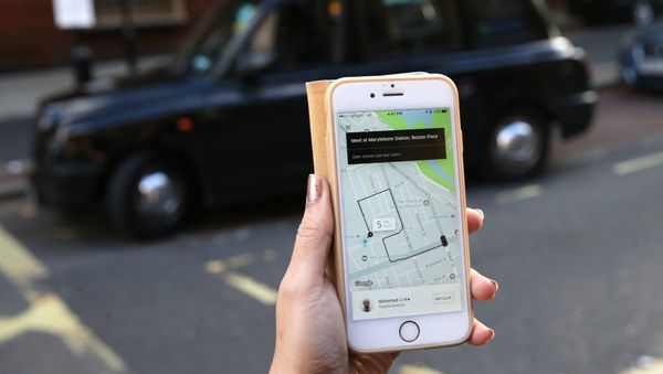 A woman poses holding a smartphone showing the App for ride-sharing cab service Uber in London on September 22, 2017 - Sputnik International