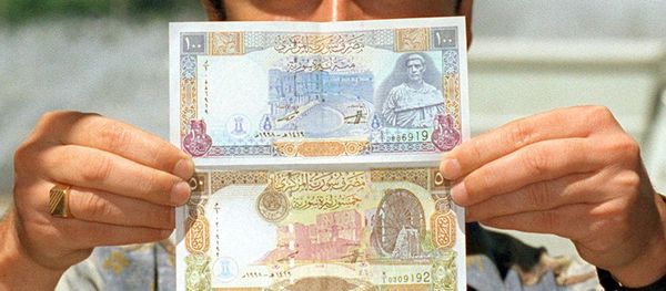 A Syrian man displays new 100 and 50 pound bills issued by the Syrian Central Bank. (File) A Syrian man displays new 100 and 50 pound bills issued by the Syrian Central Bank. (File) - Sputnik International