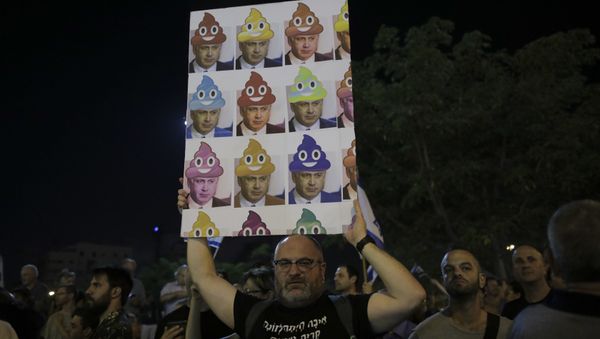 In this Saturday, Aug. 26, 2017 file photo, a man holds up a poster during a weekly protest against Israeli Prime Minister Benjamin Netanyahu, seen on the poster, in front of the home of Israel's attorney general Avichai Mandelblit, in Petah Tikva, Israel. With a slew of corruption scandals closing in on him, Netanyahu is increasingly dropping what remains of his statesmanlike persona in favor of nationalist rhetoric popular with his base. By cozying up to conservatives, anti-migrant voices and West Bank settlers, Netanyahu appears to be trying to reframe the corruption allegations as an ideological witch-hunt. - Sputnik International