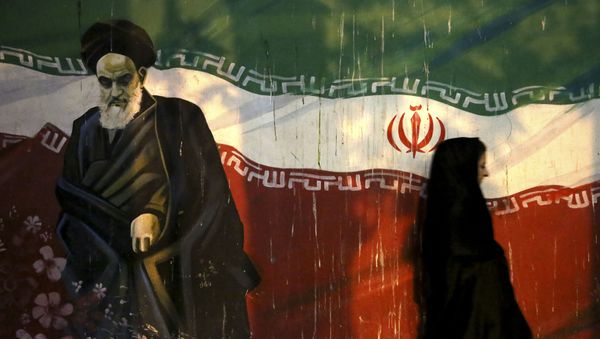 veiled Iranian woman walks past a mural depicting the late revolutionary founder Ayatollah Khomeini, and national Iranian flag, painted on the wall of the former U.S. Embassy, in Tehran, Iran - Sputnik International